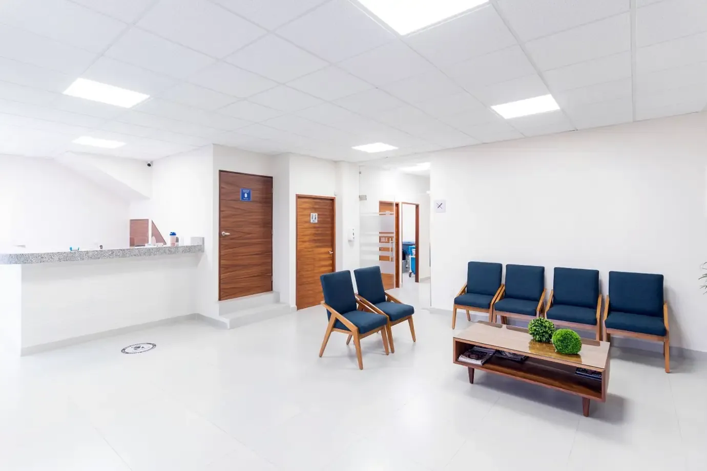 Bright, empty clinic waiting room with blue chairs and reception desk