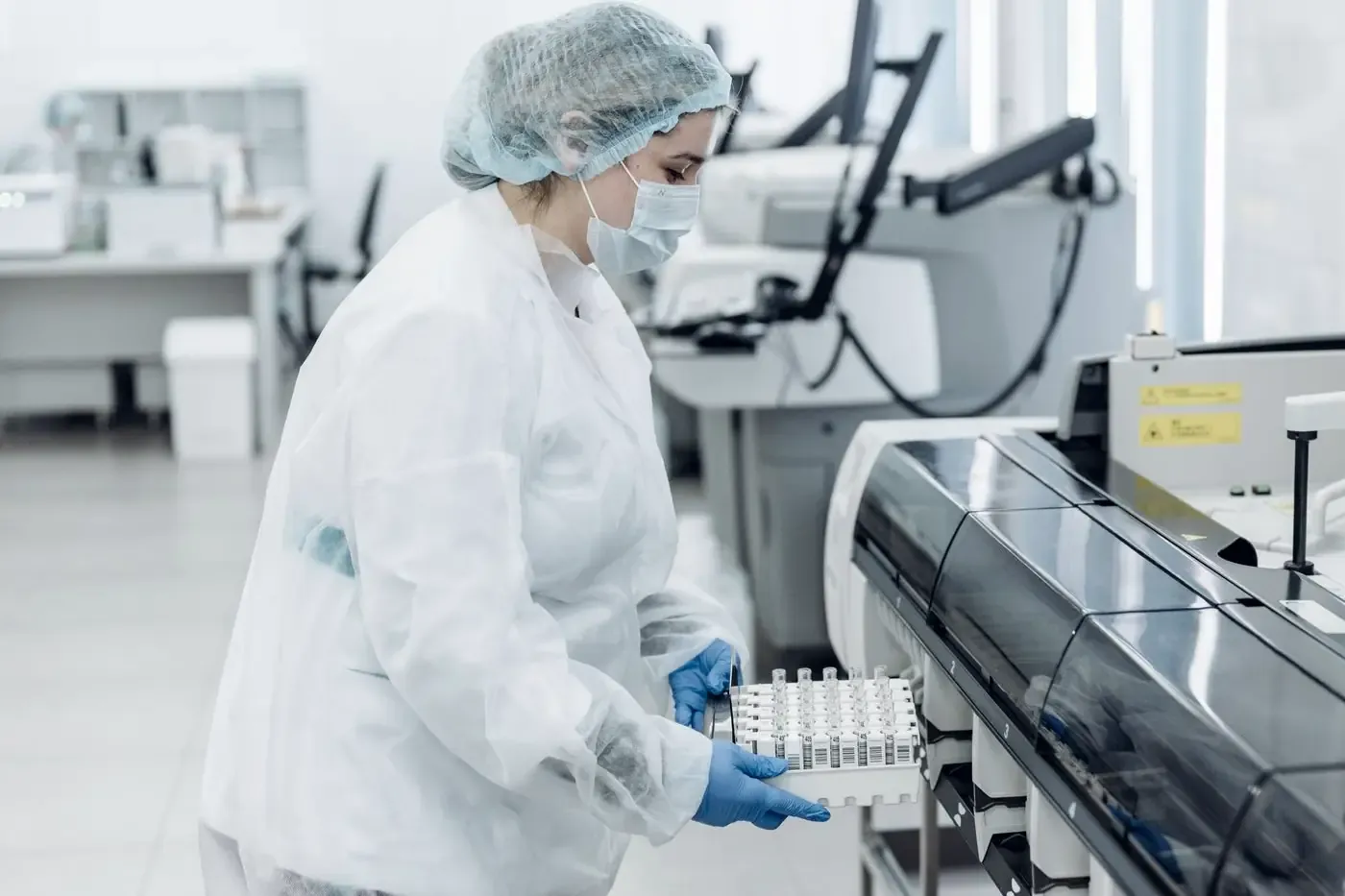 Lab technician loading a rack of blood sample tubes into an analyser