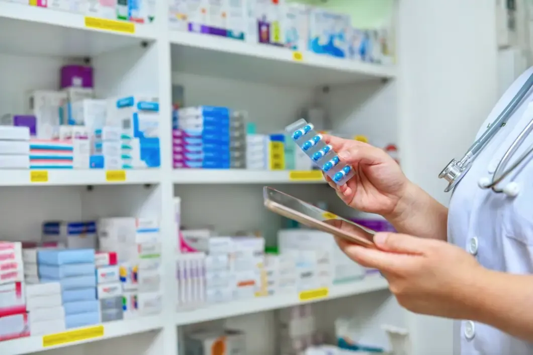 Pharmacist holding a medicine strip in front of pharmacy shelves